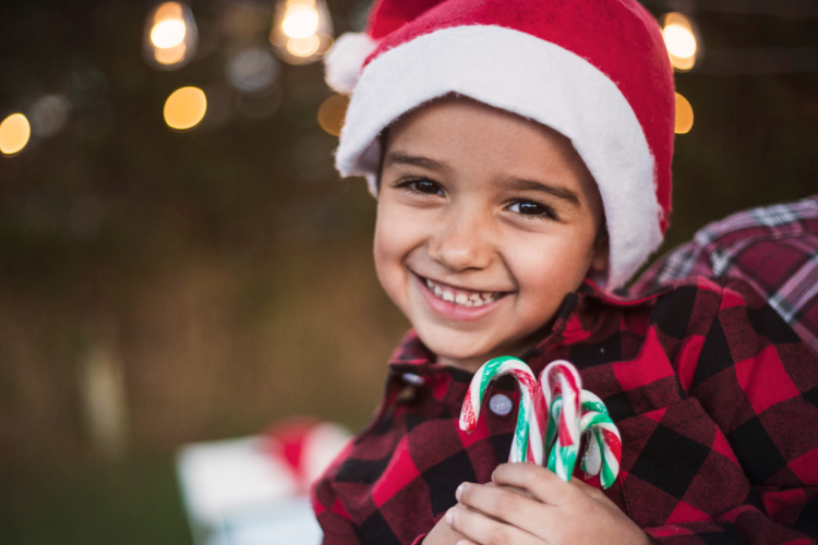 Happy little boy at Christmas with a Santa hat on holding candy canes