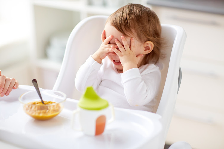 child in highchair with hands over their face