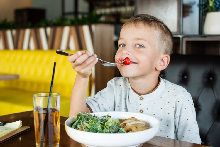 young boy sitting at the table eating salad