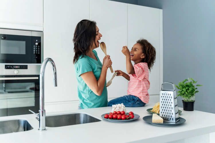 Mom eating with daughter in the kitchen. Daughter is sitting on the counter