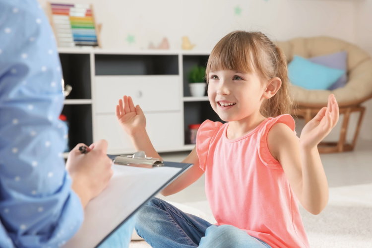 young girl smiling looking at therapist who has a clipboard in her hand