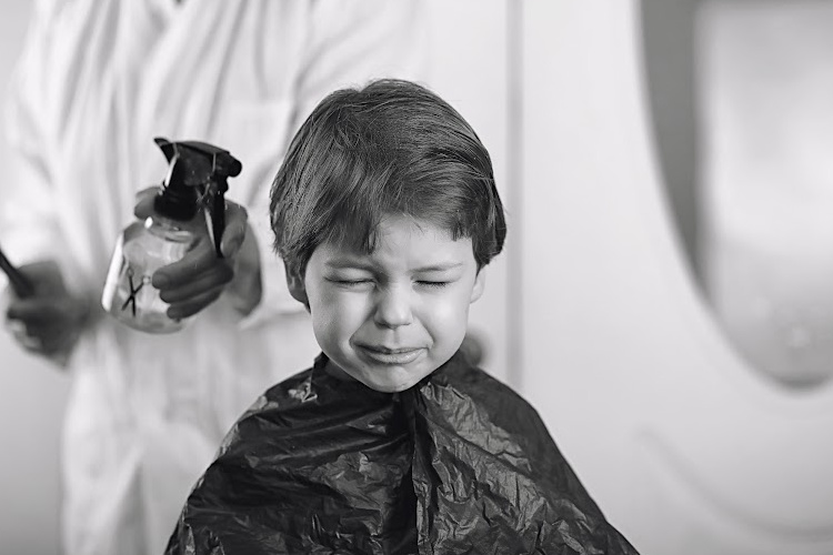 little boy sitting in the barber chair not happy about his haircut