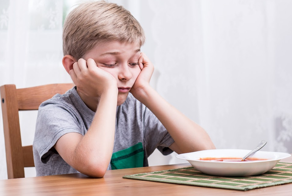 young boy sitting at the table unhappy about eating