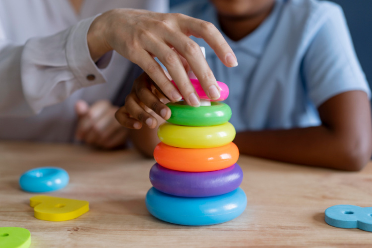 Therapist's hand on toy showing child how to manipulate the toy