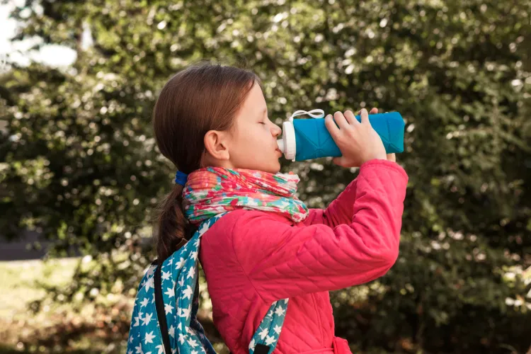 Young girl standing in front of a tree drinking from a water bottle