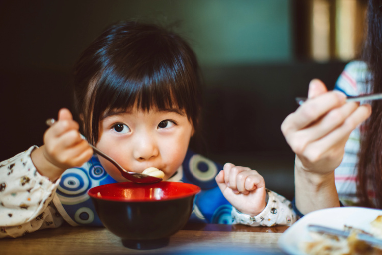 Little girl sitting at the table eating a bowl of cereal