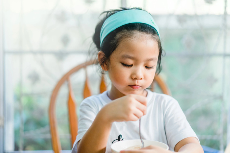 Young girl sitting at the table looking down at her breakfast - not happy