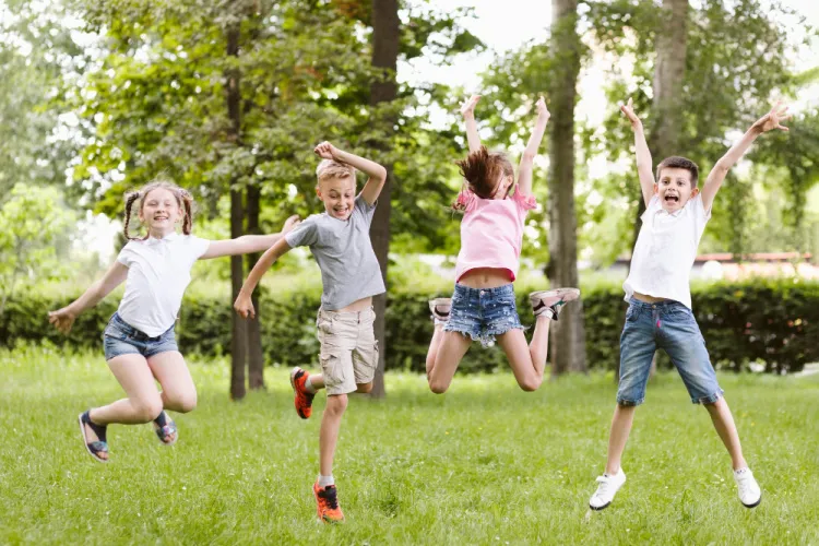 4 young kids outside at a park jumping in the air 