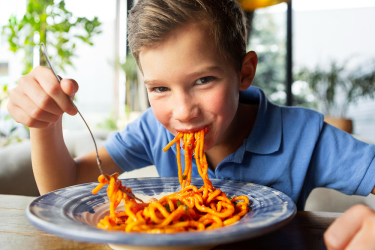 boy eating spaghetti smiling with noodles hanging from his mouth