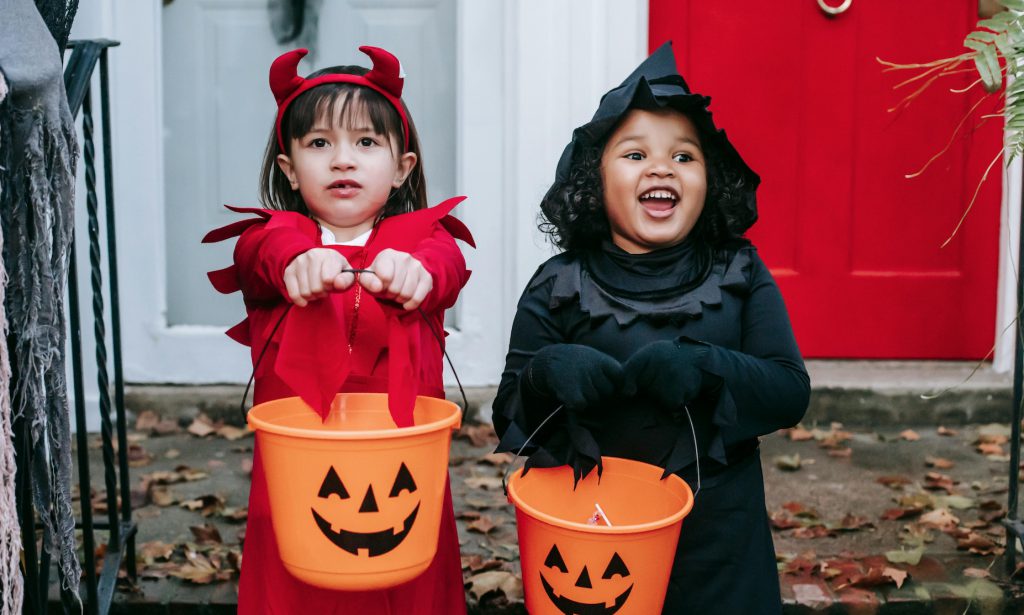Two children trick of treating on Halloween with orange pumpkin baskets.