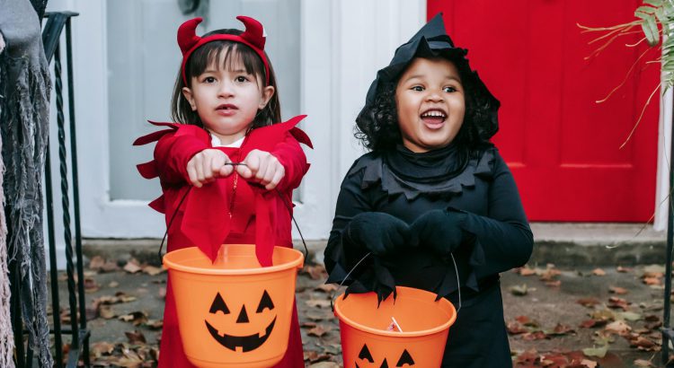 Two children trick of treating on Halloween with orange pumpkin baskets.